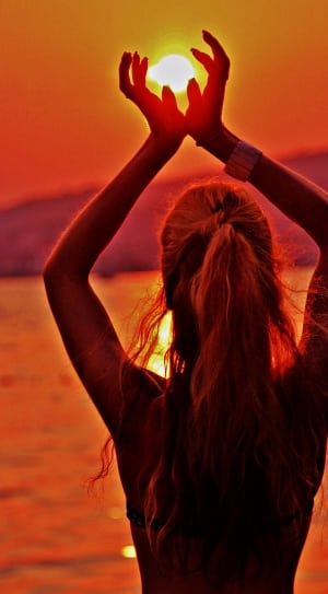 woman standing in the beach with hands cupping sun photo thumbnail
