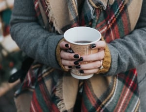 human wearing grey coat and holding disposable cup white black substance inside thumbnail