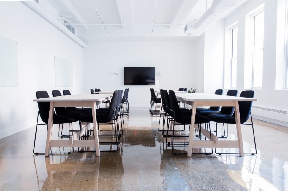 rectangular white wooden conference table with fabric chairs inside a white paint wall room with black flat screen wall mounted tv preview