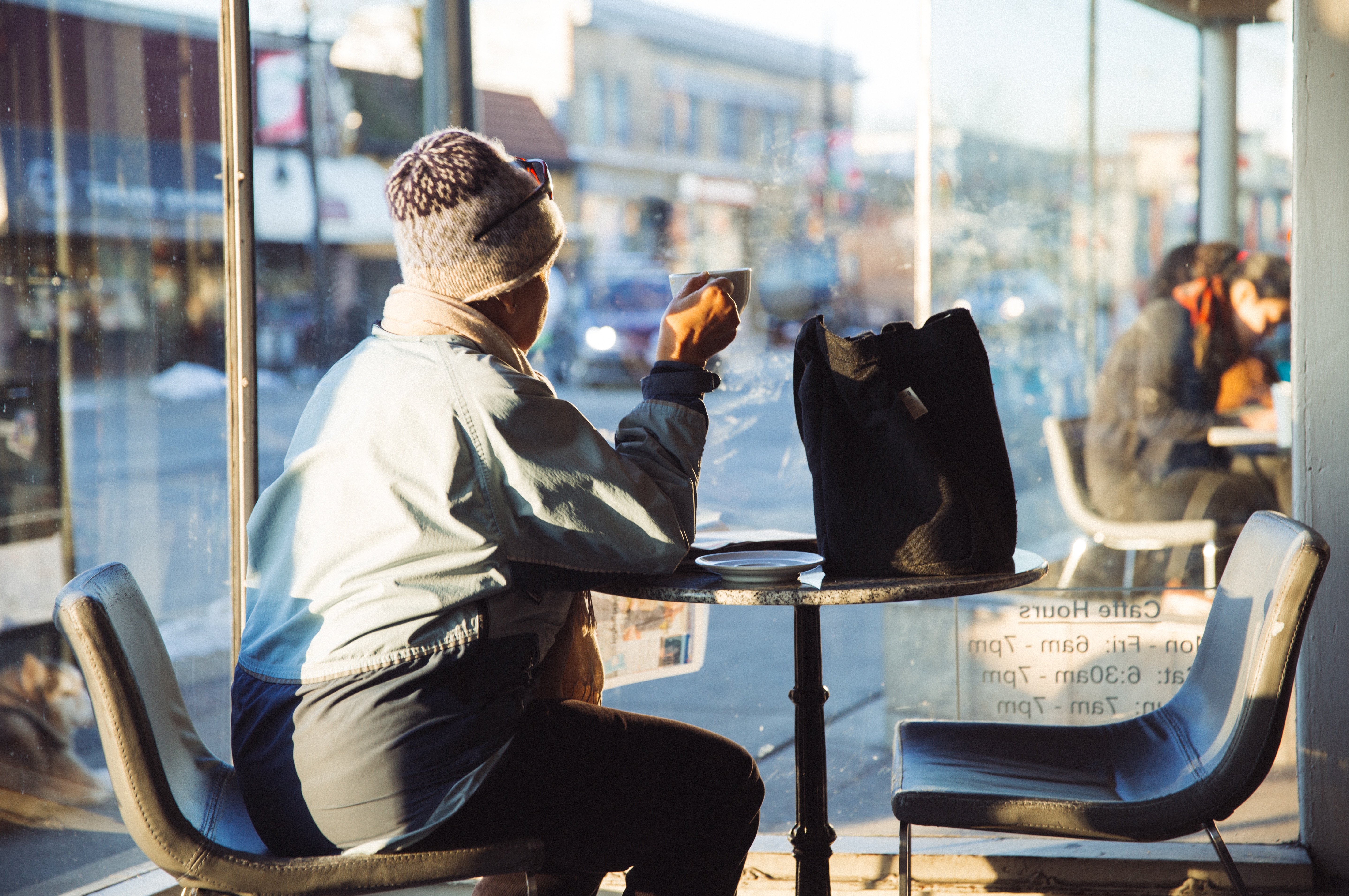 woman in blue jacket sitting on grey chair drinking coffee inside restaurant
