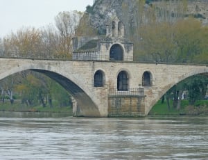 concrete bridge with building in middle above body of water thumbnail