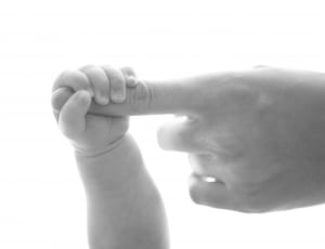 baby holding person's pink finger on grayscale photography thumbnail