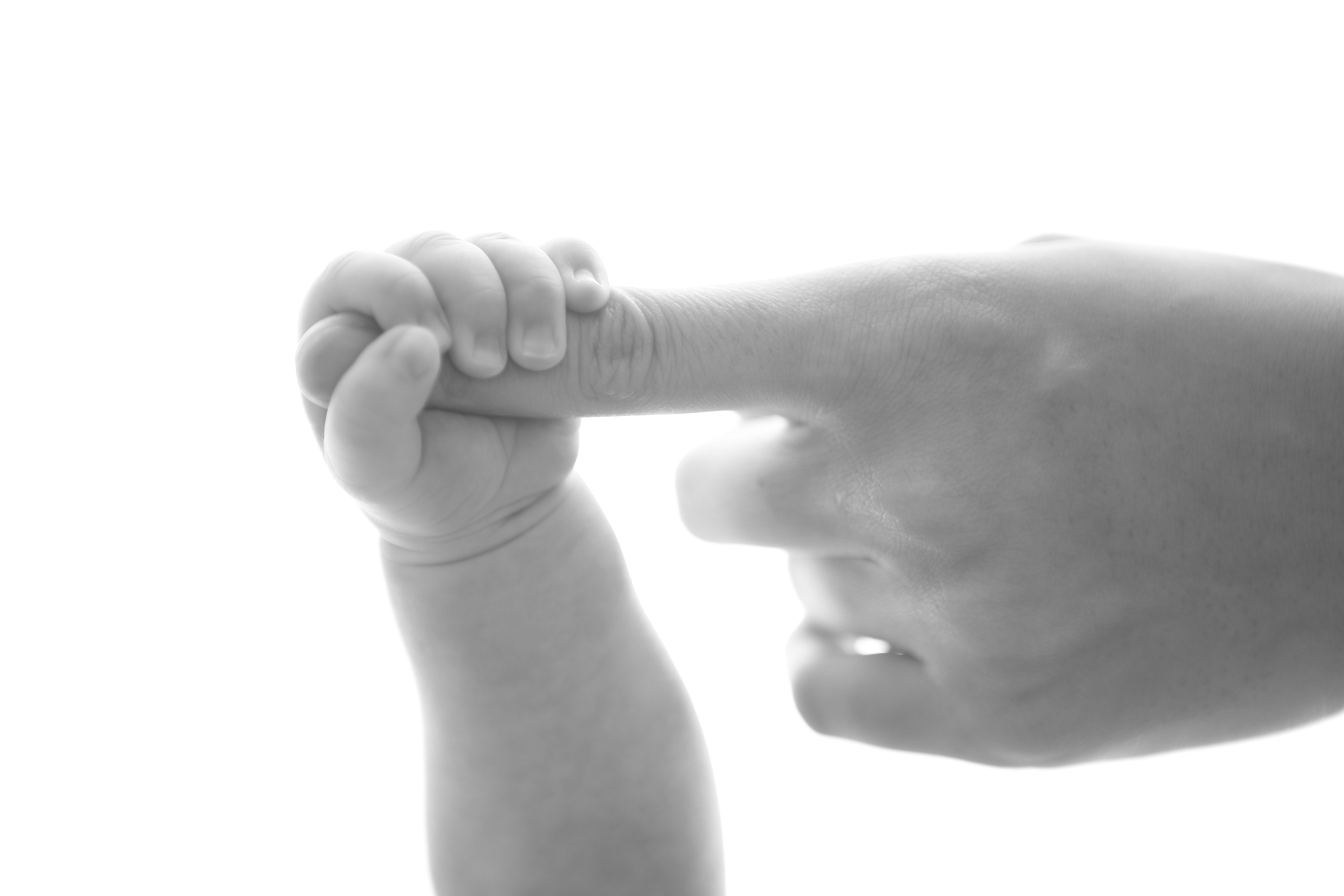 baby holding person's pink finger on grayscale photography