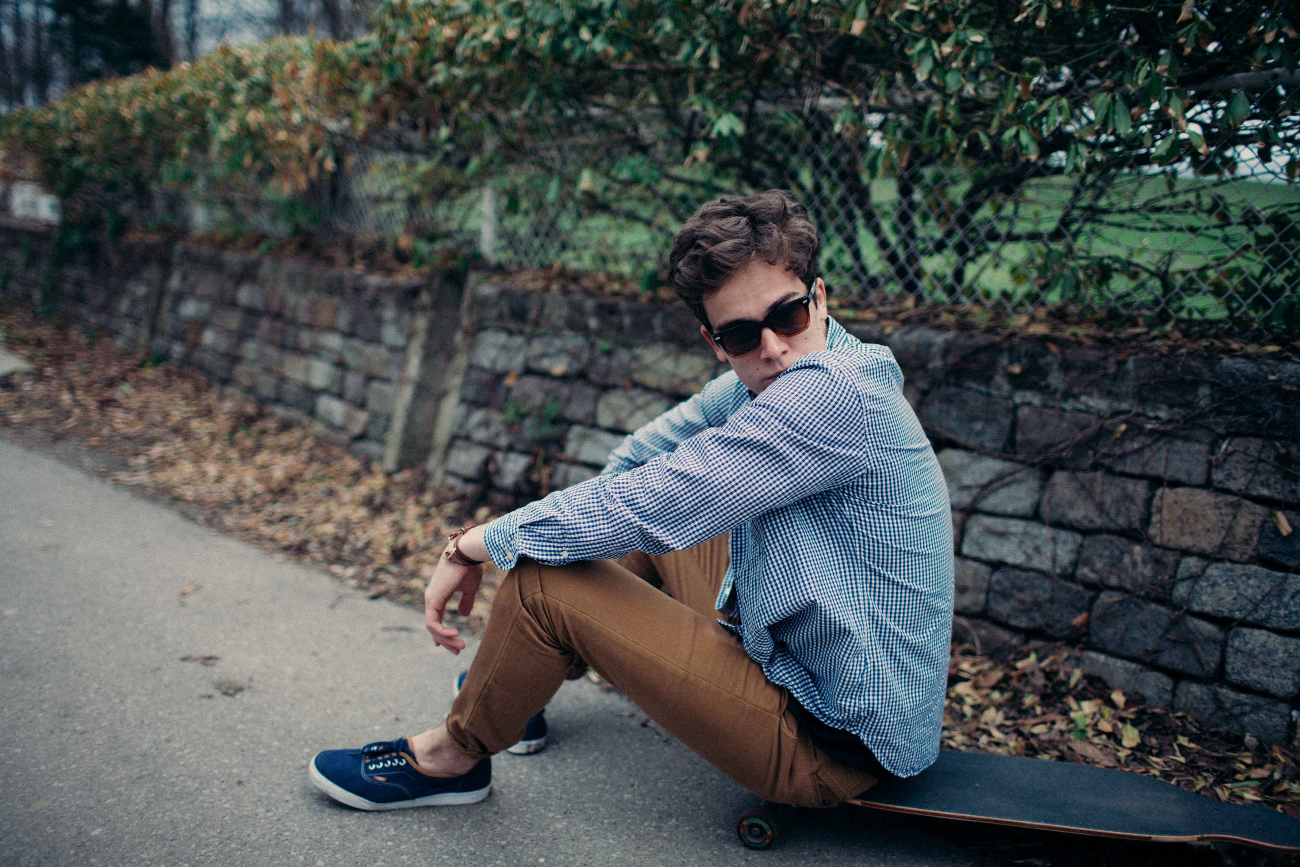 man in black sunglasses blue long sleeve sport shirt brown pants and blue  sneakers sitting on black long board during daytime free image  Peakpx