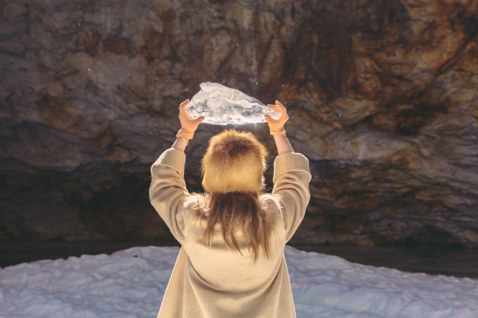 woman in brown coat carrying crystal facing cave preview