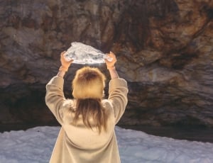 woman in brown coat carrying crystal facing cave thumbnail