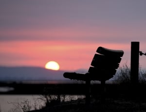brown wooden bench near river during sunset thumbnail