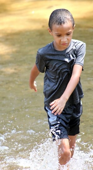 boy walking in body of water during daytime thumbnail