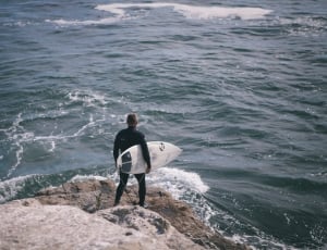 man holding surfboard near seashore during daytime thumbnail