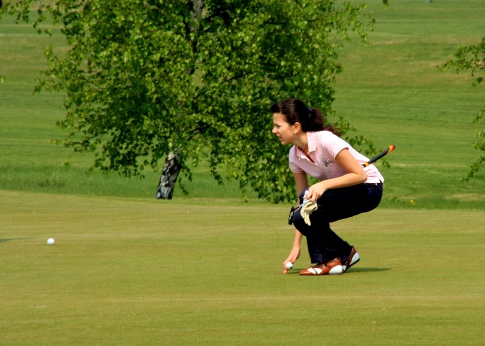 woman bending picking white golf ball on golf course preview