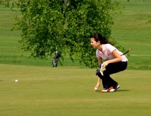woman bending picking white golf ball on golf course thumbnail