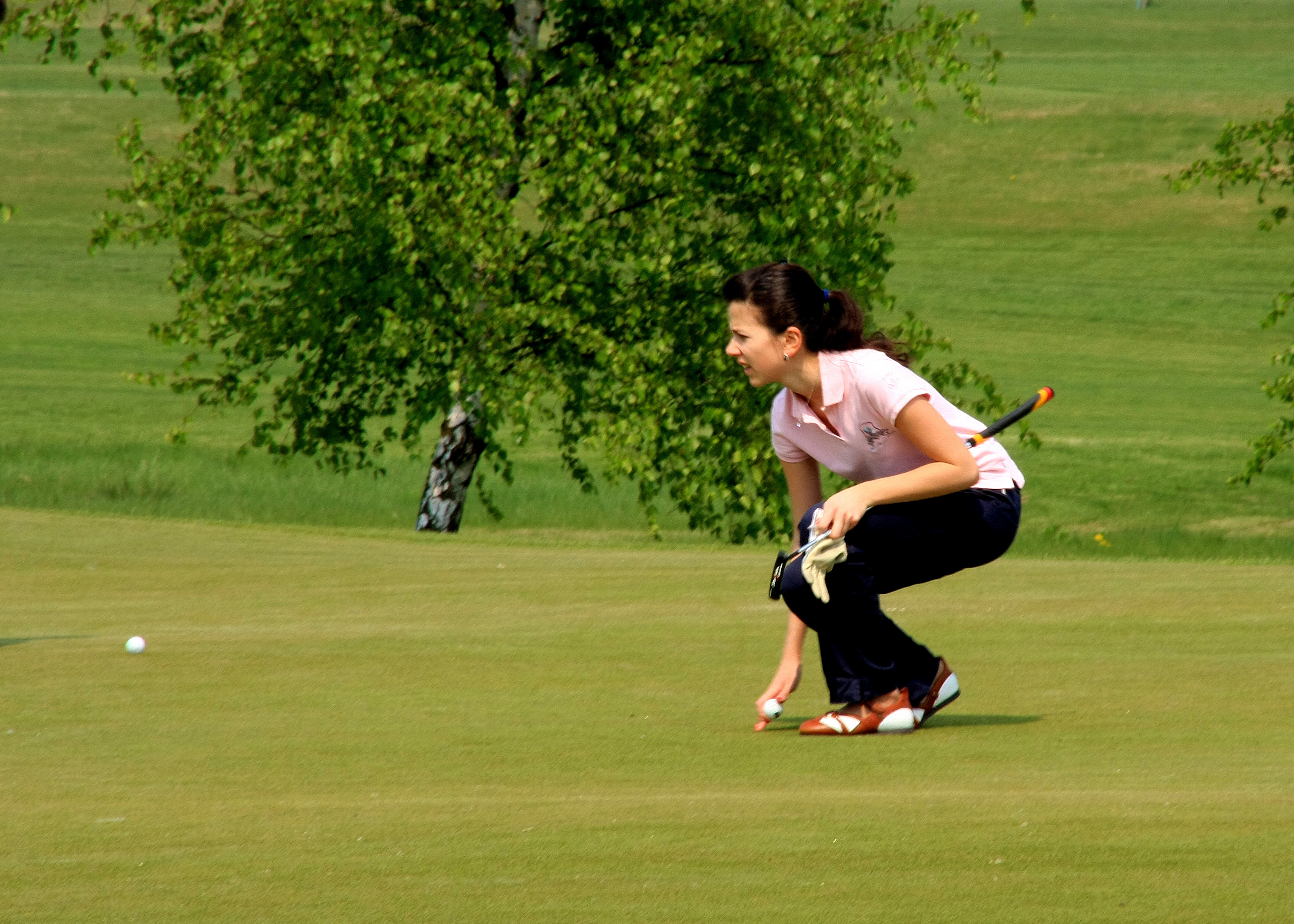 woman bending picking white golf ball on golf course