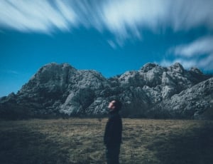 man wearing black jacket standing across gray rock formation looking on sky during daytime thumbnail