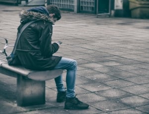 person in green parka sitting on a concrete bench thumbnail