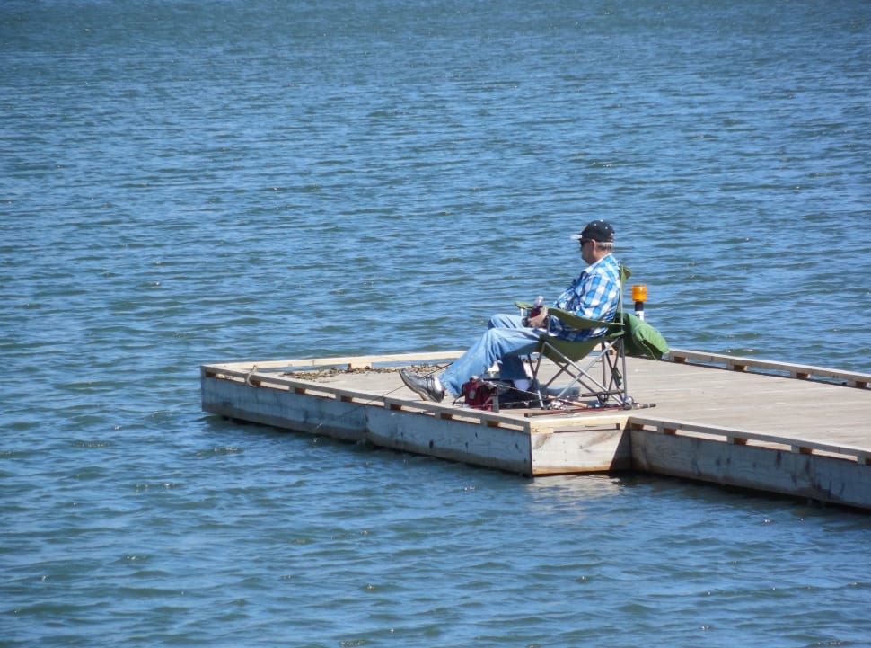 person sitting on chair on concrete sea dock during daytime preview