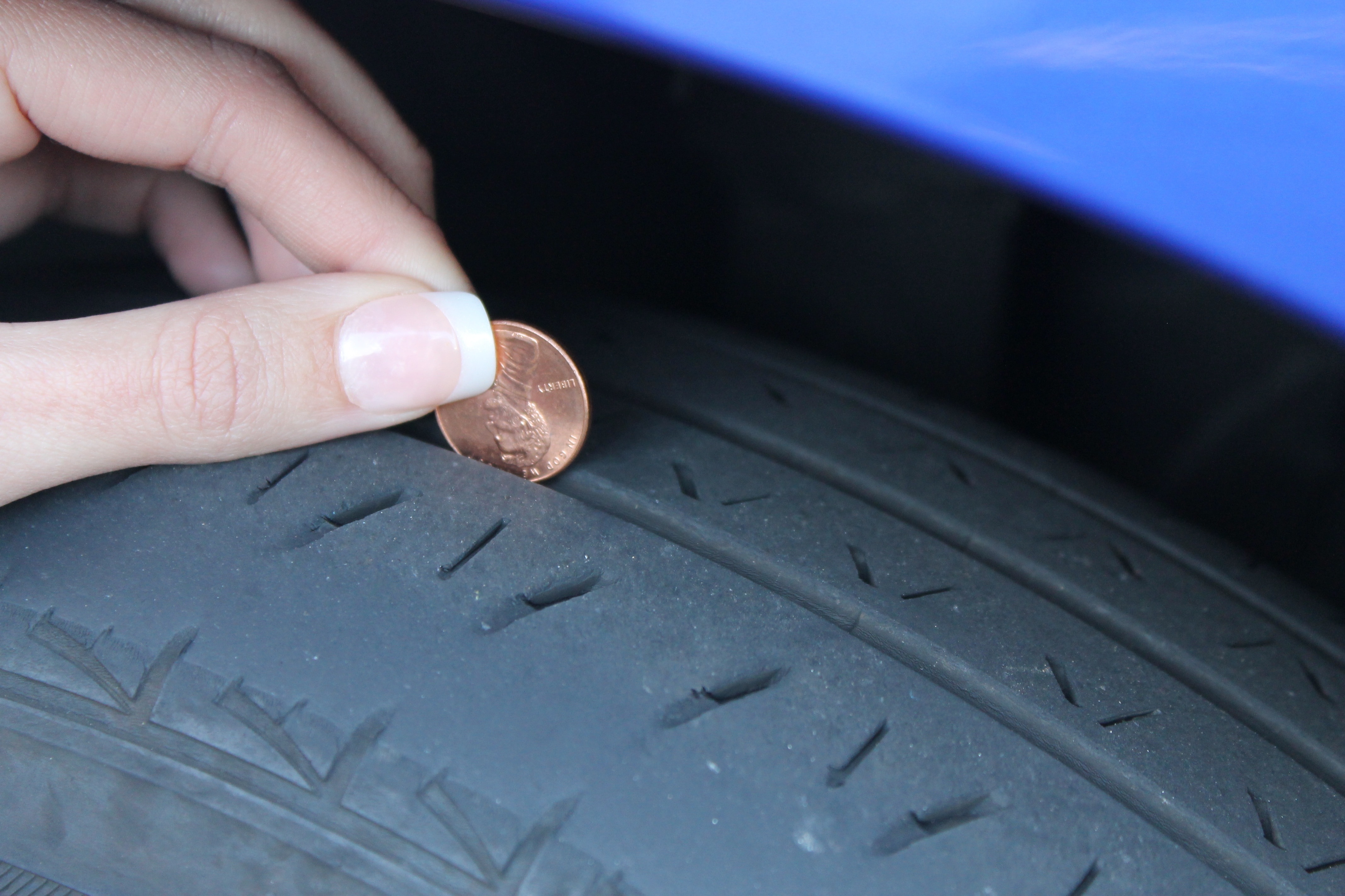 person holding coin calibrating vehicle tire