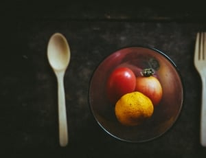red translucent footed glass with three round fruits beside silver spoon and fork thumbnail