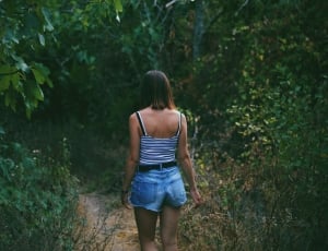 woman walking on a pathway surrounded by green trees and plants thumbnail