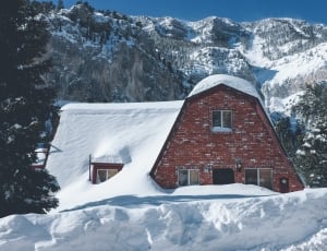 maroon concrete house covered by snow beside trees during daytime thumbnail