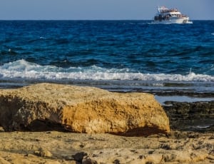 rocks on seashore with white yacht on sea thumbnail
