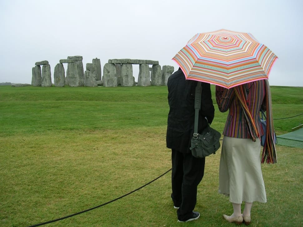 two people holding umbrella while looking to Stonehenge landmark preview