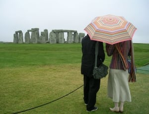 two people holding umbrella while looking to Stonehenge landmark thumbnail