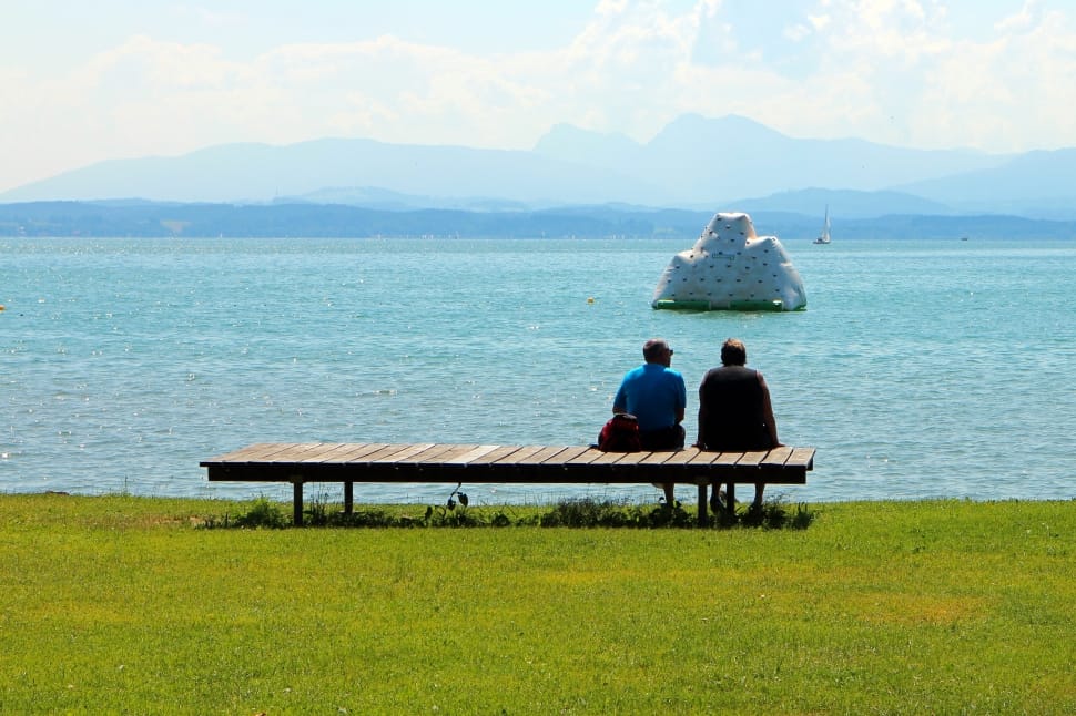 two people sitting on long brown wooden bench on a sunny day preview