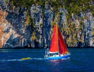red and blue sailboat near green and grey mountain thumbnail