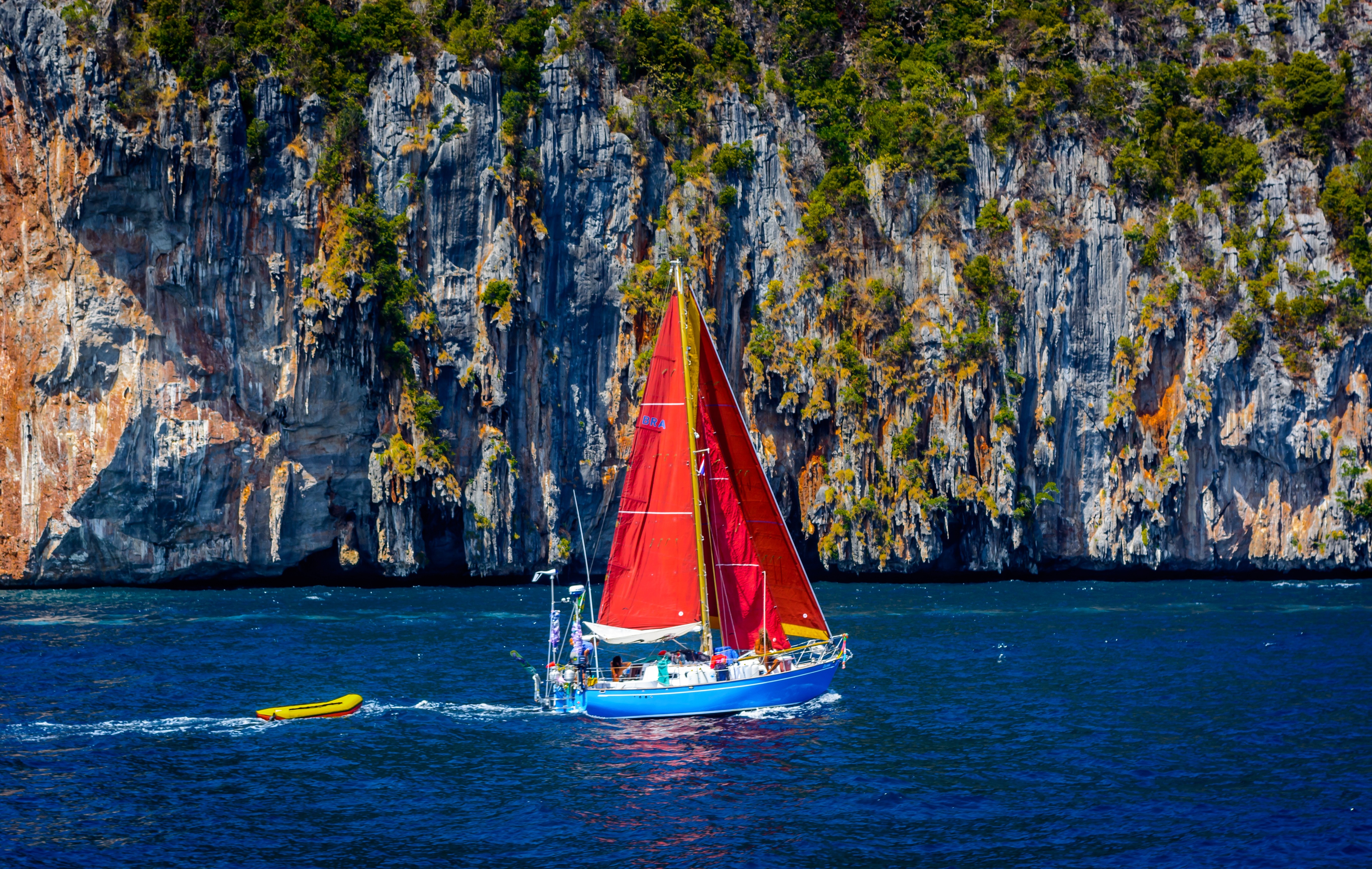 red and blue sailboat near green and grey mountain