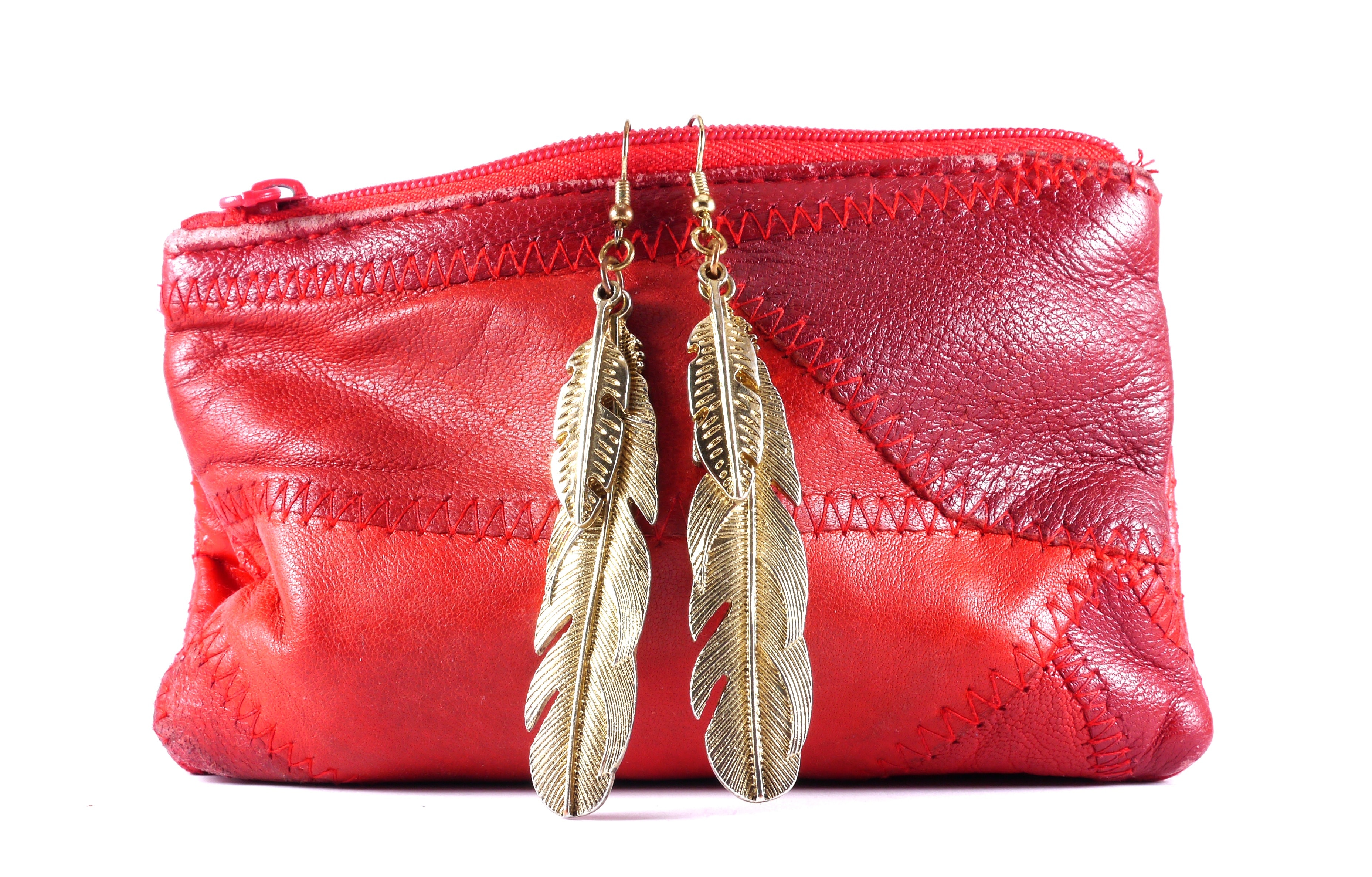 red leather purse and pair of gold dangling feather earrings