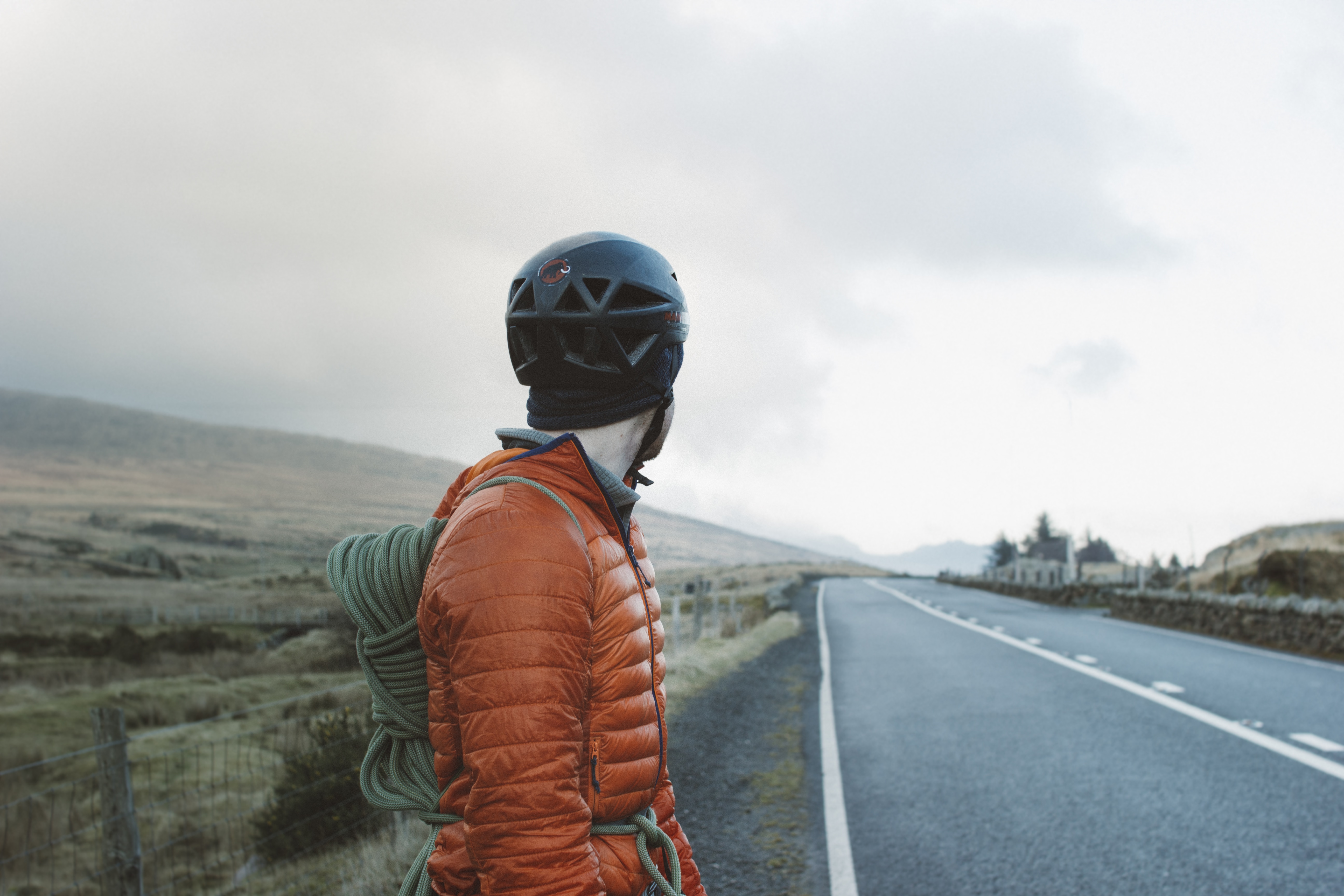 man wearing orange bubble jacket facing grey road and clouds view