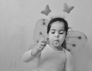 gray scale photo of girl wearing butterfly costume blowing bubbles thumbnail