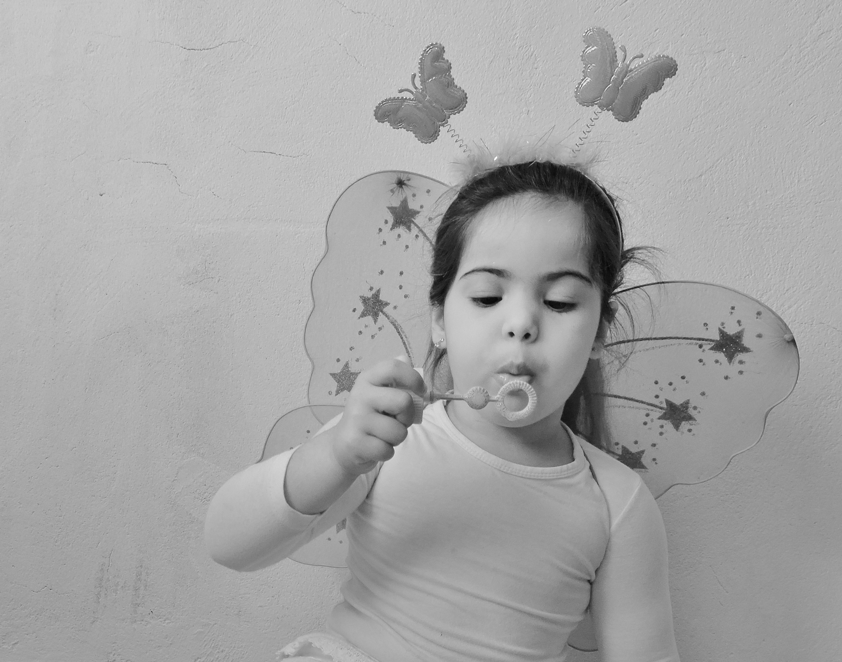 gray scale photo of girl wearing butterfly costume blowing bubbles