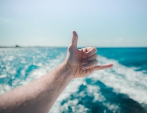 person making a hand sign near the sea during daytime thumbnail