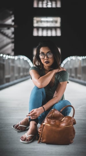 black haired woman wearing black plastic frame eyeglasses and gray t-shirt with blue skinny jeans thumbnail