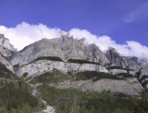 low angle photo of gray rocky mountain under blue sky and white clouds thumbnail
