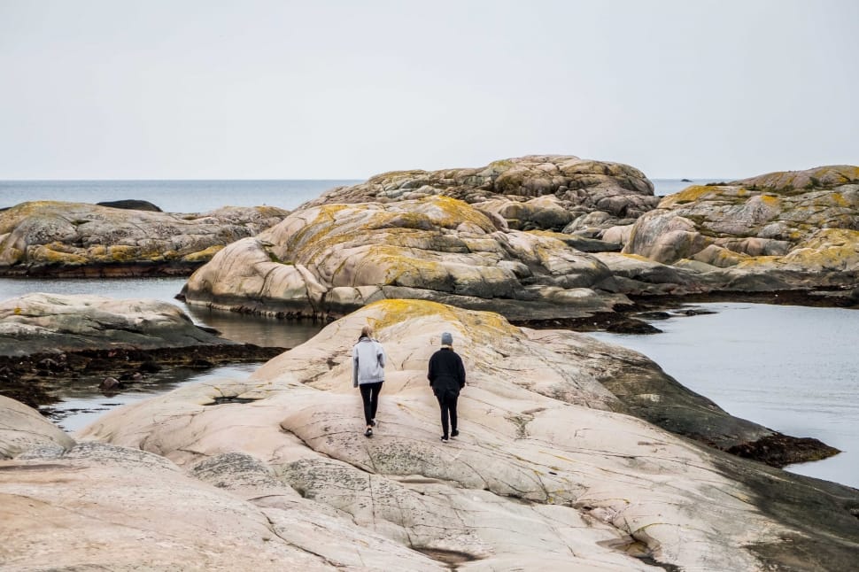 man and woman in coat walking on gray rock mountain seashore during daytime preview