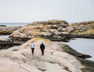 man and woman in coat walking on gray rock mountain seashore during daytime thumbnail