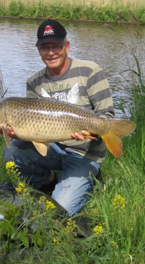 man in stripe long sleeve shirt carrying beige fish behind lake thumbnail