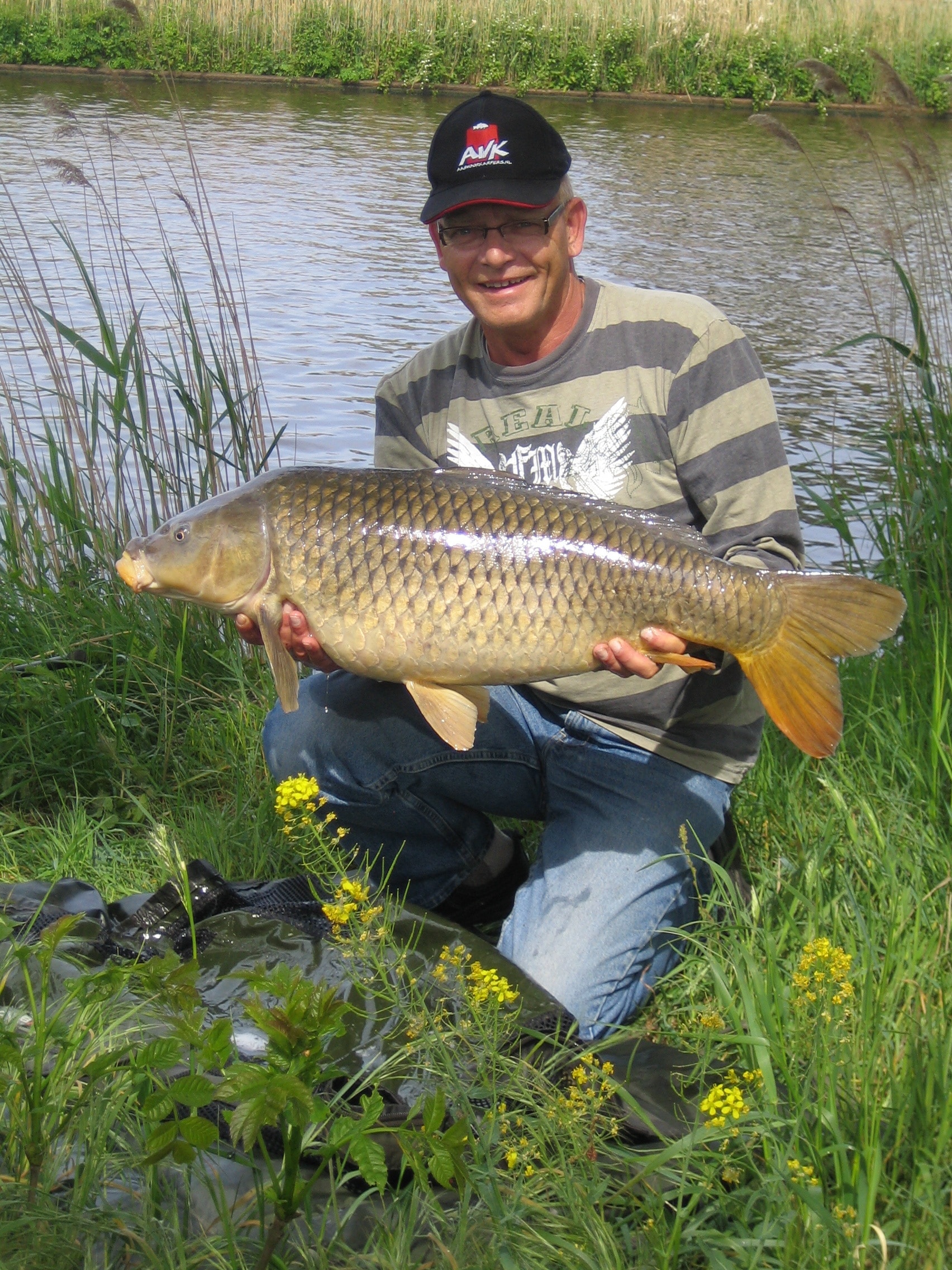 man in stripe long sleeve shirt carrying beige fish behind lake