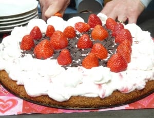 round cake topped with white icing and red strawberries thumbnail