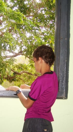 boy in pink shirt and black bottoms at window with tree outside at daytime thumbnail