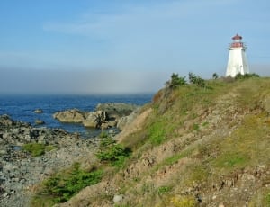 lighthouse and green grass covered mountain thumbnail