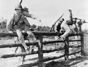 greyscale photo military men jumping wooden fence thumbnail