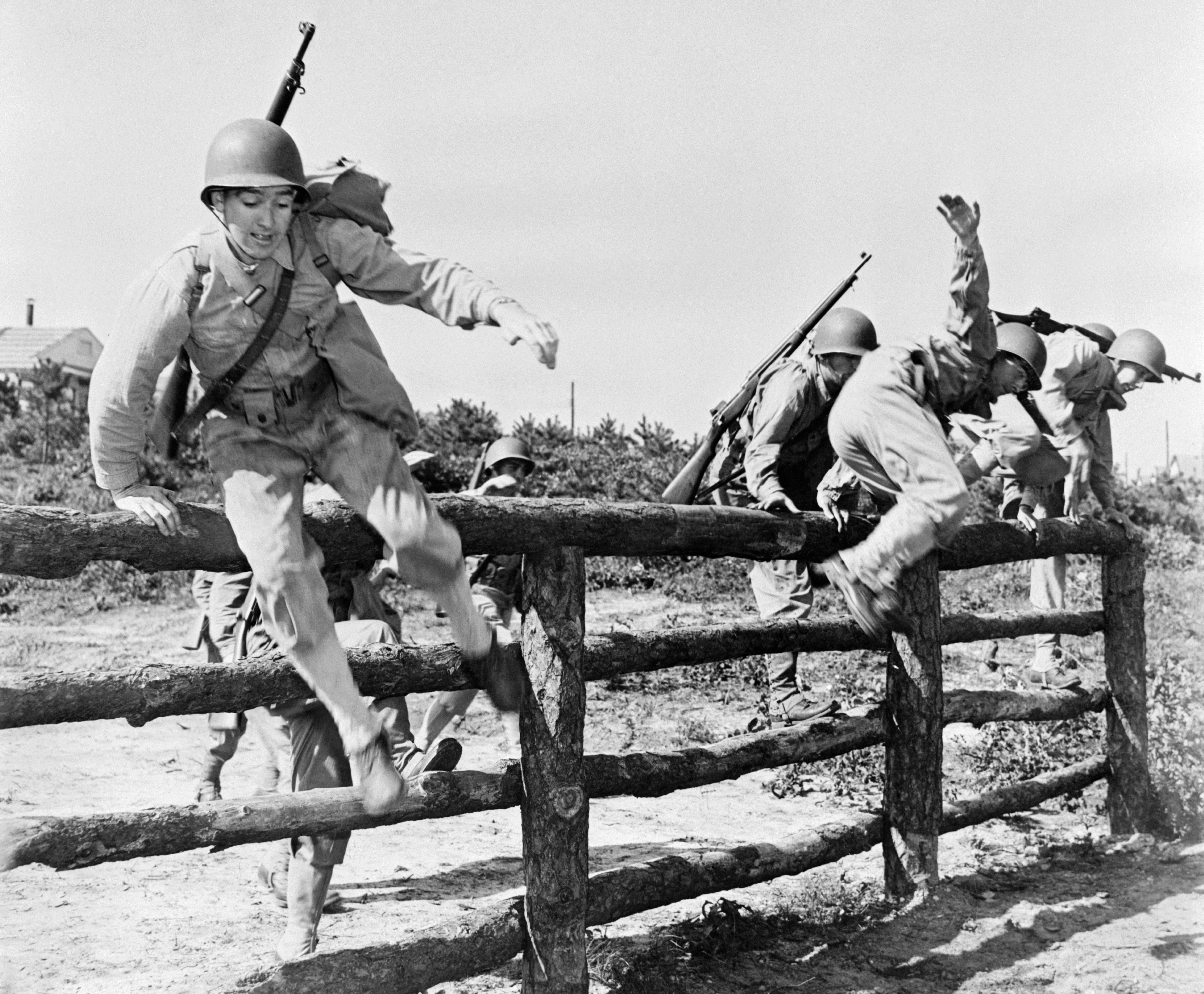 greyscale photo military men jumping wooden fence