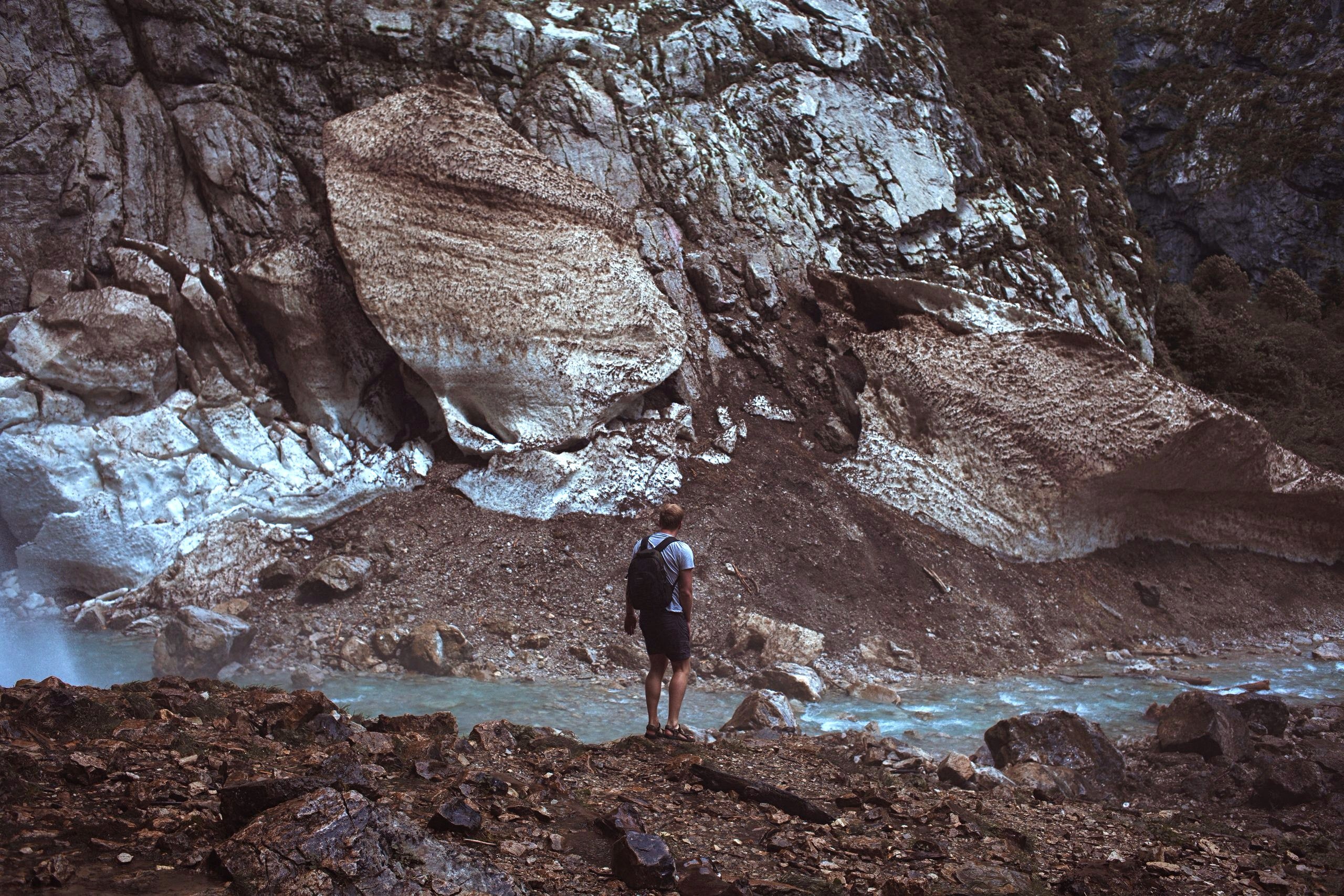 man in black backpack standing beside river