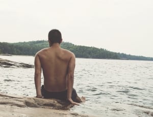 man sitting on the seashore looking on water thumbnail