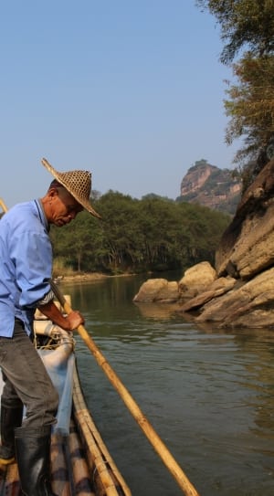 person wearing blue long-sleeve shirt paddling bamboo raft thumbnail