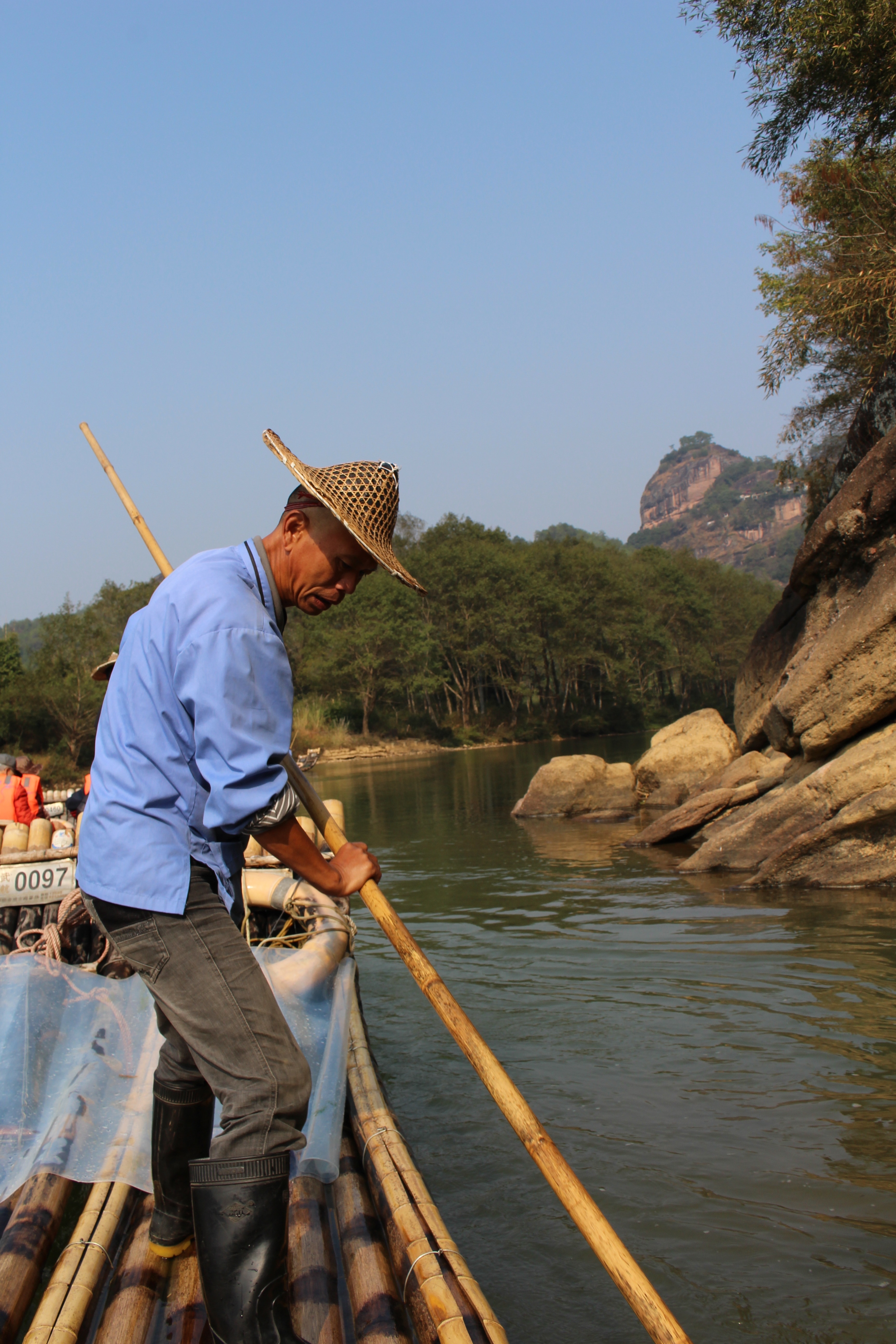person wearing blue long-sleeve shirt paddling bamboo raft