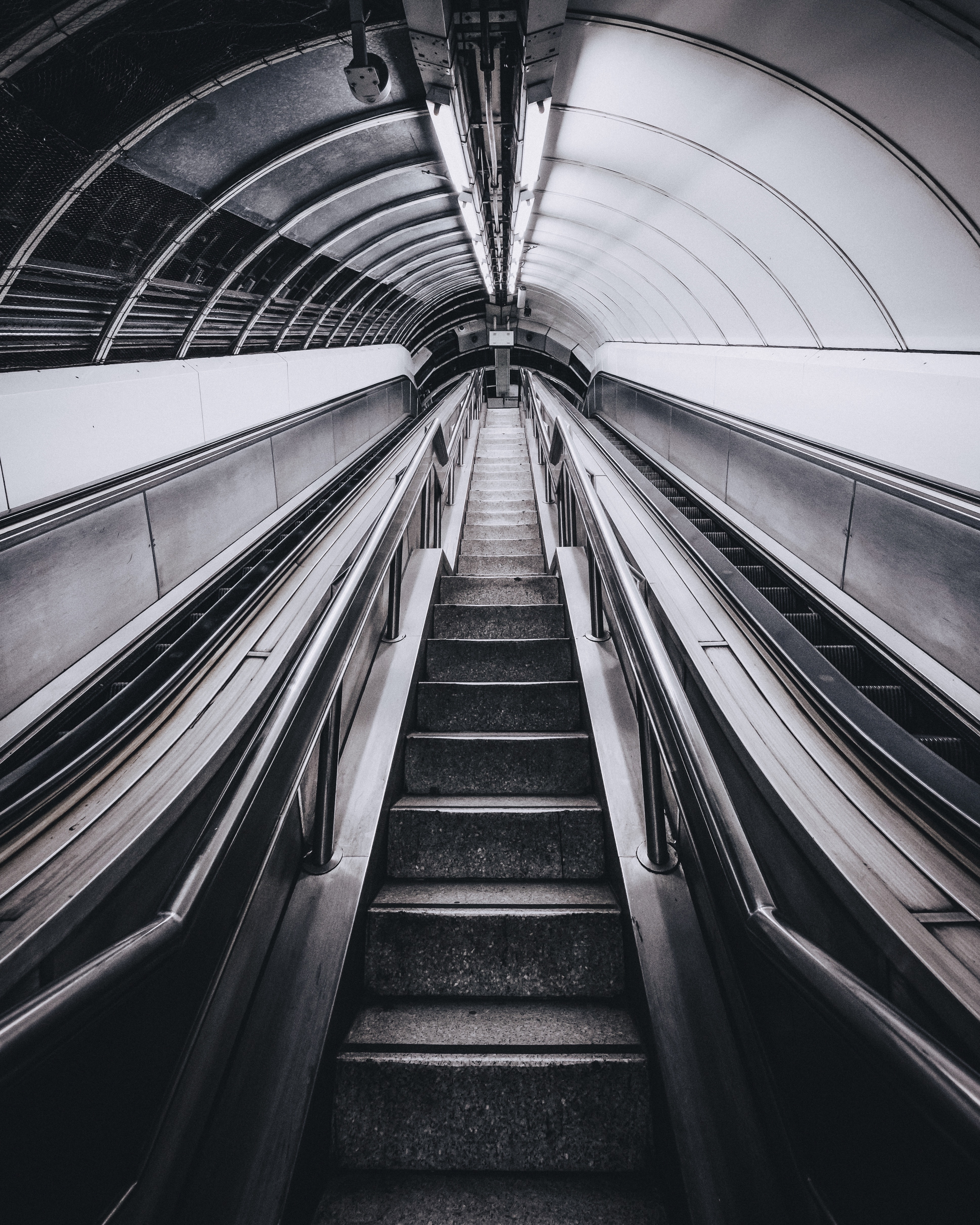 low angle greyscale photography of an escalator inside a tunnel